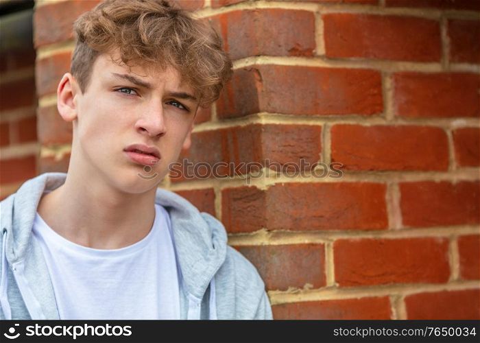 Serious male boy teenager outside leaning on brick wall wearing a gray hoody in urban city