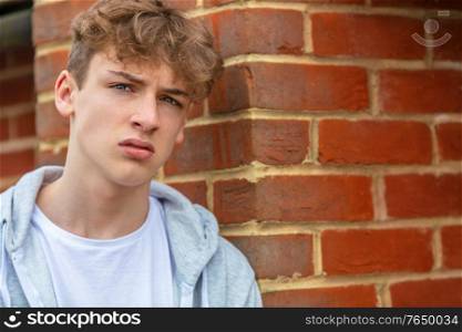 Serious male boy teenager outside leaning on brick wall wearing a gray hoody in urban city