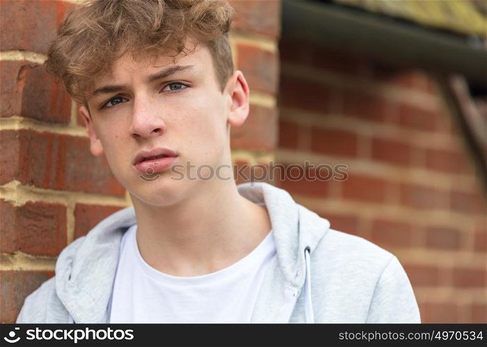 Serious male boy teenager outside leaning on brick wall wearing a gray hoody