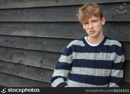 Serious male boy teenager young adult outside leaning on a wall wearing a striped jumper