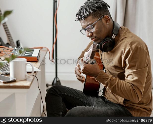 serious male musician home playing guitar mixing with laptop