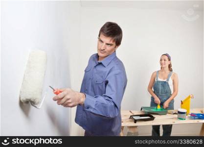 Serious man holding roller with woman in background