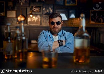 Serious man in sunglasses sitting at the counter in bar. One male person resting in pub, human emotions, leisure activities, nightlife. Man in sunglasses sitting at the counter in bar