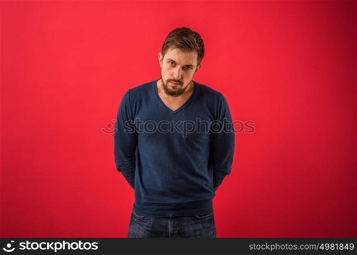 Serious man looking at camera standing against red background