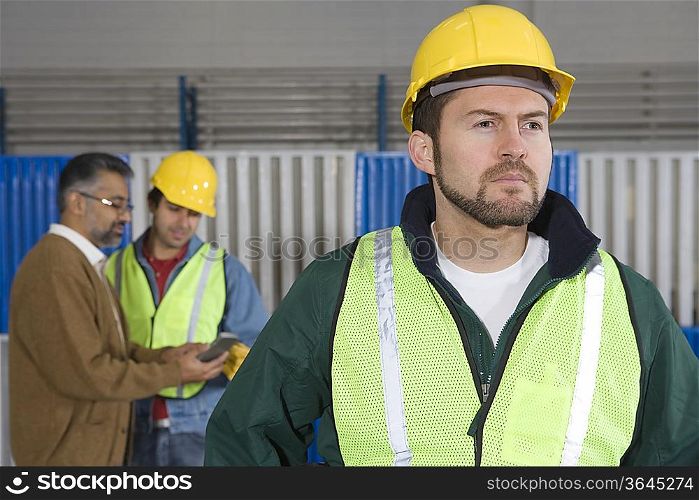 Serious man standing in factory colleagues in background