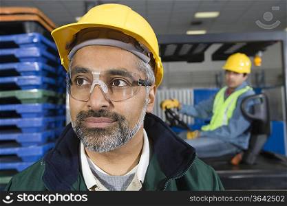 Serious man standing in factory wearing hart hat