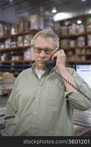 Serious man using telephone in distribution warehouse