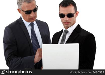 Serious men in smart suits with sunglasses holding a laptop