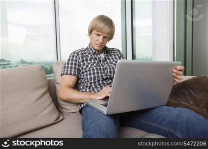 Serious mid-adult man using laptop on sofa at home