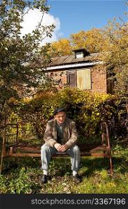 Serious middleaged man sit on old rusty bed in autumnal garden