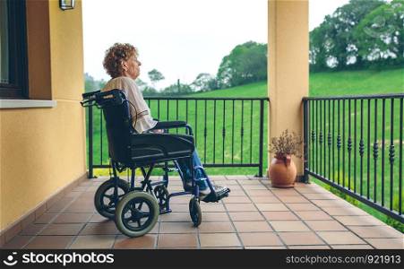 Serious older woman in a wheelchair in the porch. Older woman in a wheelchair