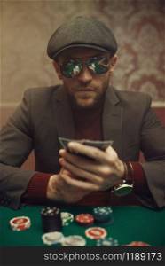 Serious poker player in sunglasses playing in casino. Games of chance addiction. Man with cards in hands leisures in gambling house. Serious poker player playing in casino