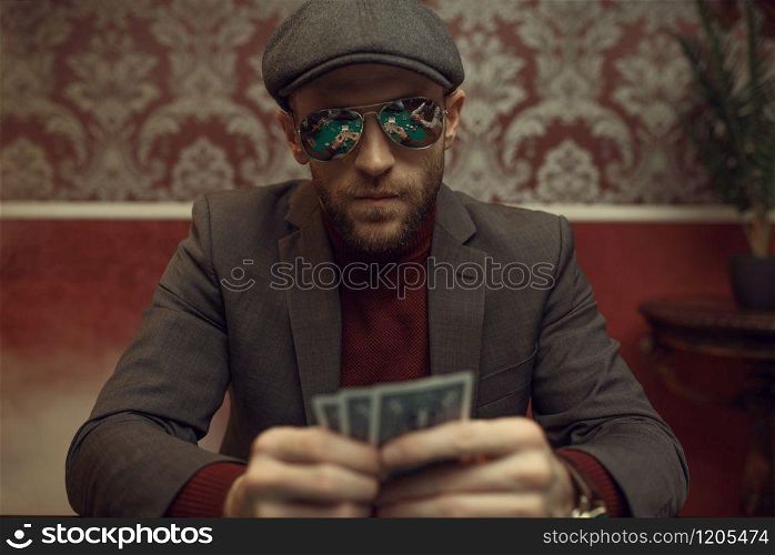 Serious poker player in sunglasses playing in casino. Games of chance addiction. Man with cards in hands leisures in gambling house