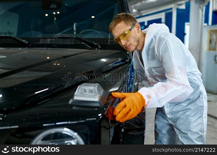 Serious repairman in protective goggles and safety clothes inspecting car vehicle painting quality. Serious repairman inspecting painting quality of vehicle