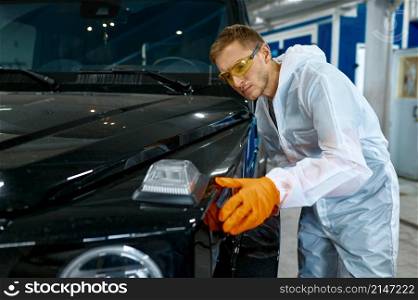Serious repairman in protective goggles and safety clothes inspecting car vehicle painting quality. Serious repairman inspecting painting quality of vehicle