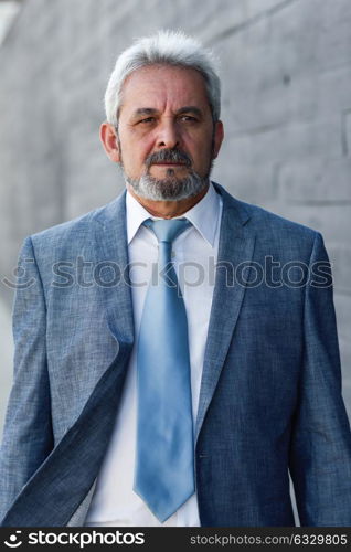 Serious senior businessman outside of modern office building. Successful business man in formal suit in urban background.