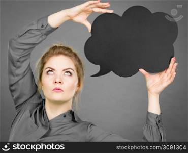 Serious student looking woman wearing grey shirt holding black thinking bubble. Serious woman holding black thinking bubble