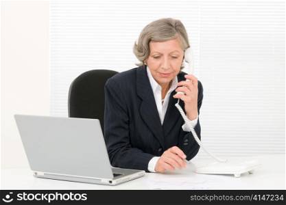 Serious successful senior businesswoman sitting behind office table portrait
