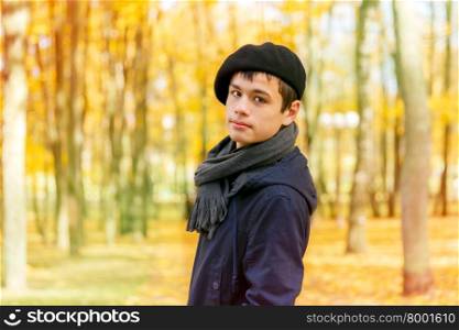 Serious teenage boy in a cap, scarf and jacket in the autumn sunny park. Toning in cool tones