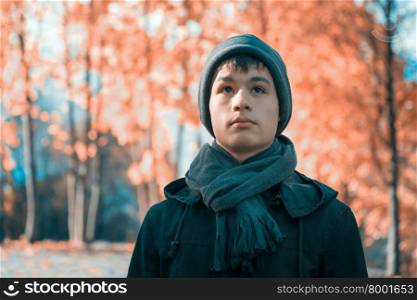 Serious teenage boy in a cap, scarf and jacket in the autumn sunny park. Toning in cool tones