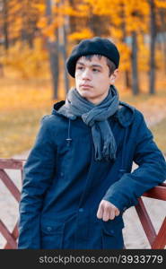 Serious teenage boy in the autumn sunny park. Serious teenage boy in a beret and jacket in the autumn sunny park