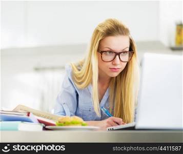 Serious teenager girl studying in kitchen