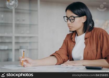 Serious woman in glasses calculates monthly expenses, taxes sitting at workplace desk in office. Focused businesswoman freelancer calculating finance, money, working on business project.. Businesswoman in glasses calculates monthly expenses, taxes sitting at workplace desk in office