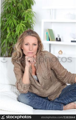 Serious woman sitting crossed legged on a white sofa