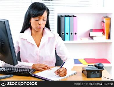 Serious young black business woman writing at desk in office