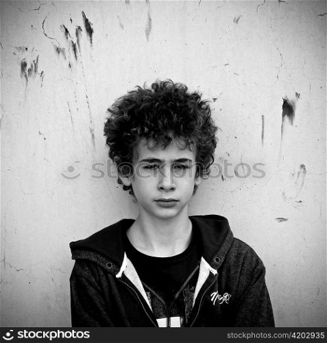 Serious young boy leaning against urban wall.