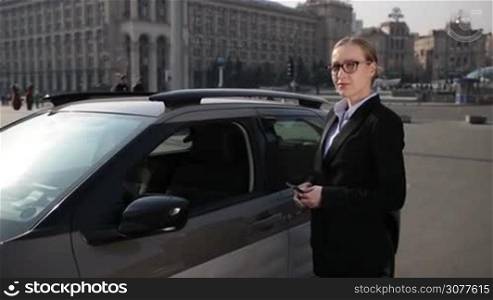 Serious young businesswoman in stylish eyeglasses and formal wear opening car door and getting into automobile. Business woman adjusting car rearview mirror before driving. Slow motion