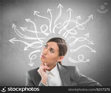 Serious, young businesswoman looking at many twisted arrows on the concrete wall overhead
