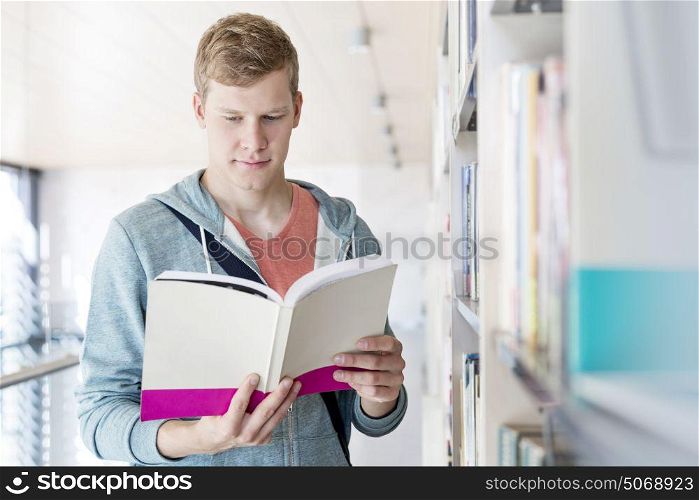 Serious young man reading book at university library