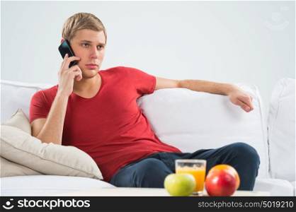 Serious young man sitting on sofa and calling with his smart phone