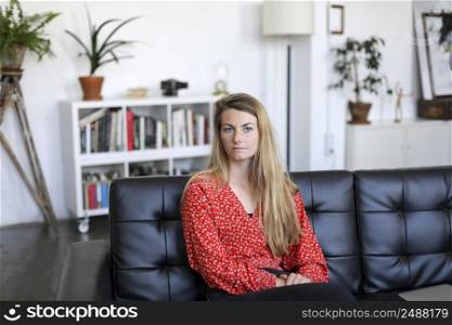 Serious young woman or teenage girl sitting on sofa at home