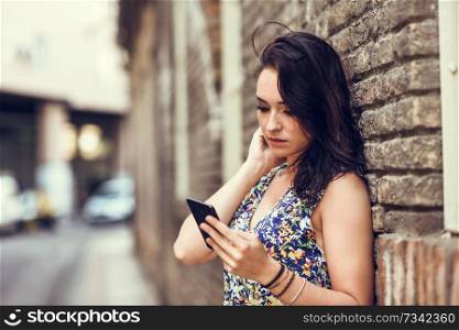 Serious young woman using her smart phone outdoors. Girl wearing flower dress in urban background. Technology concept.. Serious young woman using her smart phone outdoors. 