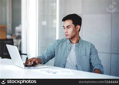 Seriously Young Businessman Working on Computer Laptop in Office. Sitting on Desk with Thoughtful Posture. Concentrated and Smart Men