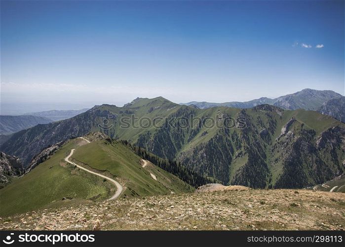 Serpentine highway in Tian Shan mountains. Green valley with blue sky and white clouds.