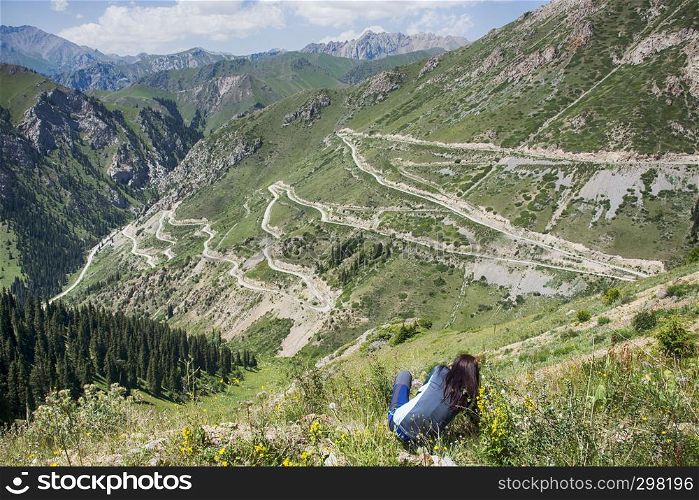 Serpentine highway in Tian Shan mountains. Spectacular landscape of mountain valley with sitting girl on the front.
