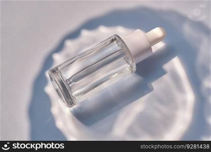 Serum bottle on a blue background. A perfect demonstration of the moisturizing properties of a serum.. Serum bottle on a blue background with glare.