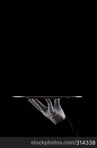 Servant wearing white glove holds stainless steel tray on black background