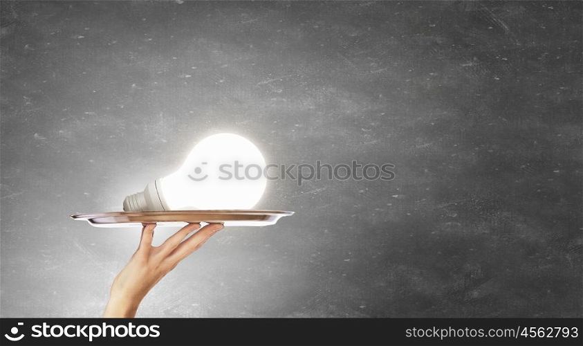 Serve idea on tray. Hand holding tray with glowing glass light bulb