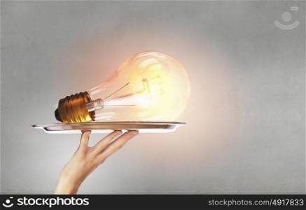 Serve idea on tray. Hand holding tray with glowing glass light bulb