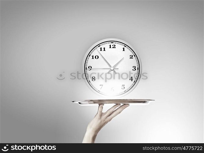 Serve time on tray. Waiter holding silver platter with white alarm clock