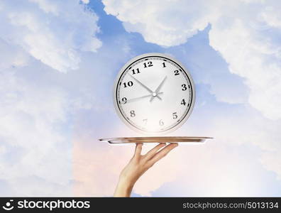 Serve time on tray. Waiter holding silver platter with white alarm clock