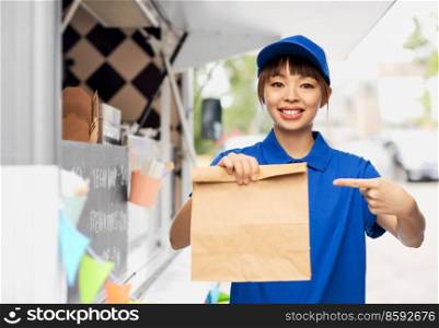 service and job concept - happy smiling delivery woman in blue uniform with paper bag over food truck on street background. delivery woman with takeaway food in paper bag