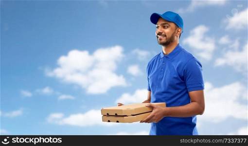 service and people concept - happy indian delivery man with pizza boxes in blue uniform over sky and clouds background. happy indian delivery man with pizza boxes in blue