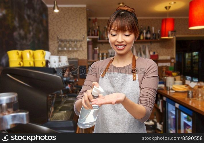 service, hygiene and health concept - happy smiling female barista or waitress in apron applying hand sanitizer or liquid soap over bar counter at restaurant background. barista with hand sanitizer or soap at restaurant