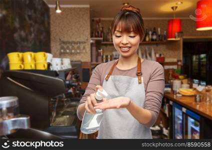 service, hygiene and health concept - happy smiling female barista or waitress in apron applying hand sanitizer or liquid soap over bar counter at restaurant background. barista with hand sanitizer or soap at restaurant