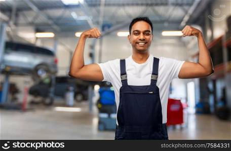 service, profession and gesture concept - happy smiling indian mechanic showing his power over car shop background. indian mechanic showing his power at car shop